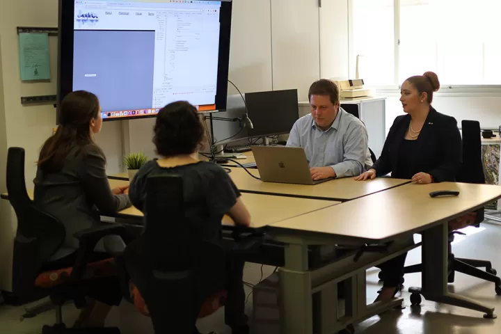 Four people sitting around a table with a laptop and a large display screen