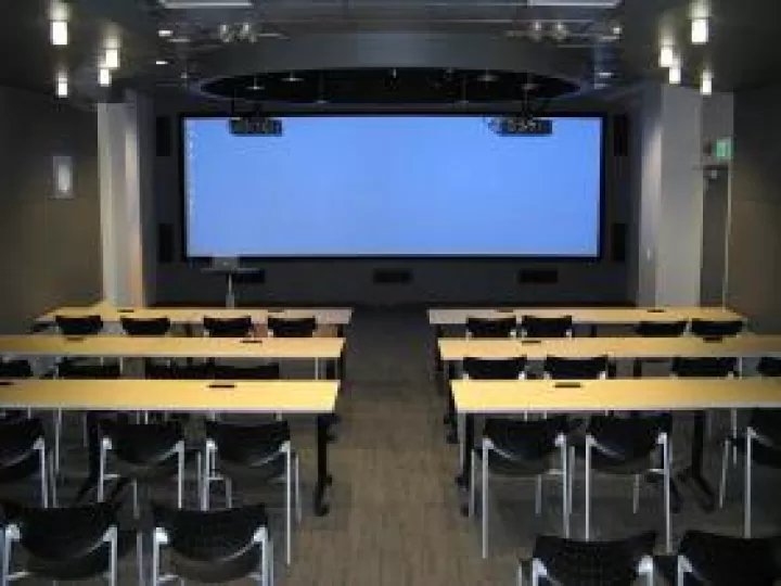 A room with tables and chairs facing a screen