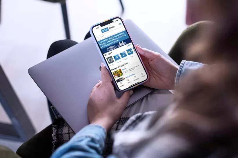 Hands holding a cell phone showing the UCLA Mobile App